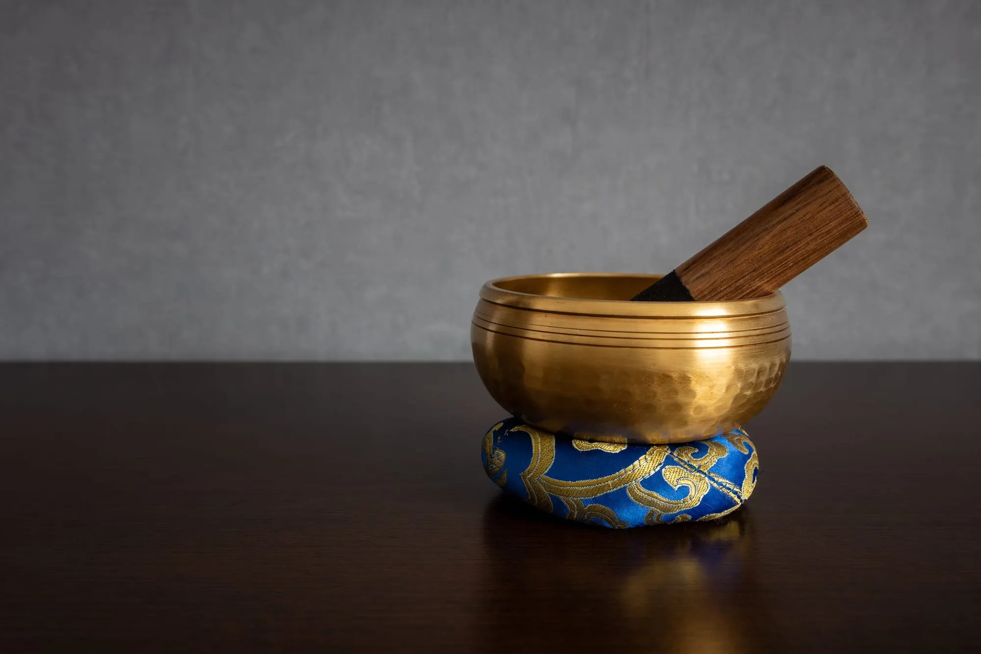 Goldene Klangschale mit Klöppel auf einem blauen Kissen